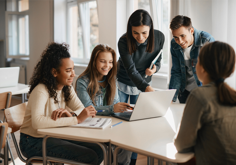 Male and female students in a class room looking at a computer with their female teacher