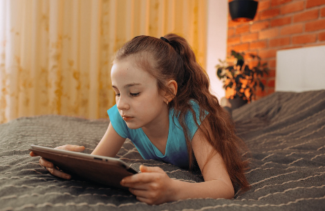 Young girl laying on bed working on tablet.