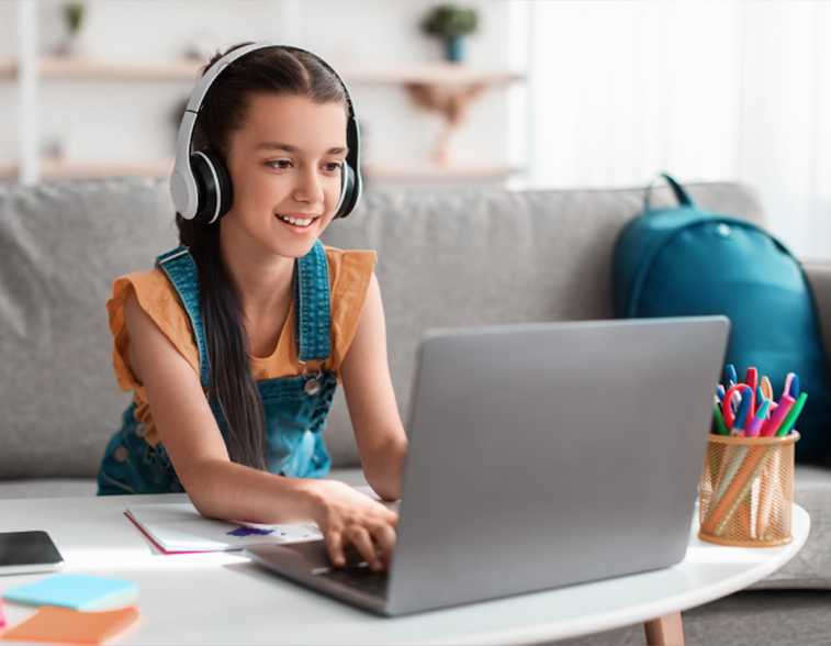 Young girl wearing headphones working on laptop on couch in home.